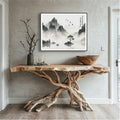 Soaring Birds Over Solitary Green Amid the Misted Peaks ink painting in a black frame above a driftwood console table in a natural wood entryway.