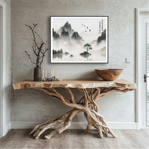 Soaring Birds Over Solitary Green Amid the Misted Peaks ink painting in a black frame above a driftwood console table in a natural wood entryway.
